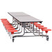 A long National Public Seating cafeteria table with red stools on it.