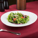 A Sushia triangular porcelain salad plate with salad on a table.