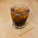 A beige Hoffmaster beverage napkin under a glass with a straw and brown liquid.