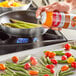 A person spraying vegetables on a pan with Vegalene Zesty Garlic spray.