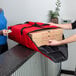 A man and woman using a red Cambro Pizza Delivery GoBag to hold pizza boxes.