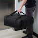 A man holding a black Cambro Insulated Pizza Delivery GoBag.