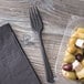 A plastic container of food next to a black compostable plastic fork.