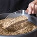 A person using a Choice clear plastic utility scoop to pour mixed white and brown grains into a plastic container.