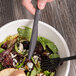 A hand holding a black Eco-Products compostable plastic knife over a bowl of salad.