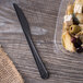 A plastic container with food and a black compostable plastic knife on a table.