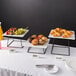 An Acopa black metal display stand with trays of food on it.