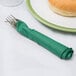A fork and knife on a white plate with a Hunter green napkin wrapped around the fork.