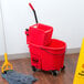 A Rubbermaid red mop bucket on a wood floor.