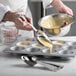 A person using Vollrath stainless steel measuring spoons to pour batter into a muffin tin.