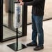 A man standing next to a glass door holding a black wet umbrella bag.