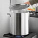 A person using a Choice large silver stock pot with a lid on a stove.