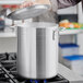 A person using a Choice aluminum stock pot with a lid on a stove.