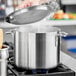 A hand holding a lid over a silver stock pot on a stove.