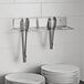 An Edlund Smart Tong Holder with tongs on a shelf.