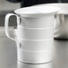 A white metal Vollrath measuring cup on a table.