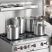 A man standing near a stove with Choice aluminum stock pots and covers.