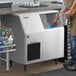 A man using a blue scoop to pour ice into a Hoshizaki undercounter ice machine.