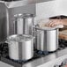 A person cooking food in a large aluminum stock pot on a stove.