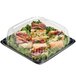 A Sabert plastic square catering tray with sandwiches and greens in it.