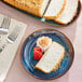 A slice of coconut-flavored pound cake served with whipped cream, toasted coconut, and a strawberry on a blue plate.