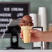 A hand holding a JOY flat bottom ice cream cone filled with ice cream.