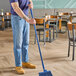 A man using a blue Carlisle Sparta broom handle to sweep a wooden floor.