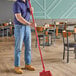 A man using a Carlisle red threaded broom handle to clean a restaurant floor.