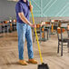A man using a Carlisle yellow threaded fiberglass broom handle to sweep the floor in a cafeteria.