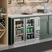 A stainless steel underbar height glass door back bar refrigerator filled with various beverages.