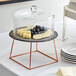 An Acopa rose gold wire cake display stand with a slate plate of grapes and crackers on it.