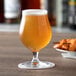 A Reserve by Libbey Belgian beer glass on a table next to a plate of food.