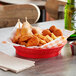 A red Tablecraft diner platter basket filled with fried food on a table.