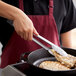 A person using Vollrath stainless steel utility tongs to cook chicken in a pan.