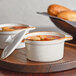 Two Acopa white stoneware casserole dishes with lids filled with soup on a tray.