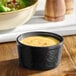 A black stoneware ramekin filled with a creamy sauce or dressing.