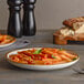 A plate of pasta with sauce and basil on an Acopa vanilla bean stoneware plate.