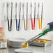 A person using Vollrath Jacob's Pride stainless steel tongs with assorted colored Kool-Touch handles to serve corn on a plate.
