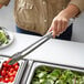 A person using Vollrath stainless steel tongs to serve cherry tomatoes at a salad bar.