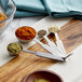 A cutting board with Vollrath stainless steel measuring spoons and different spices on it.