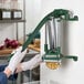A wall-mounted green metal French fry cutter being used to slice a potato.