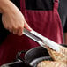 A person using Vollrath Jacob's Pride stainless steel scalloped utility tongs to serve food