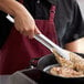 A person using Vollrath Jacob's Pride stainless steel tongs to cook food in a pan.