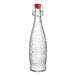 A clear glass Libbey Glacier oil, vinegar, or water bottle with a red wire bail lid.