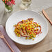 An Acopa Matte White Stoneware coupe plate with food, vegetables, and sauce on a table.