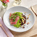 An Acopa matte white stoneware coupe plate with food and a fork on a table.