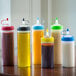 A group of Tablecraft squeeze bottles filled with pink and yellow liquids on a counter.