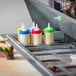 A row of Tablecraft squeeze bottles with red, blue, and green lids on a counter in a food truck interior.