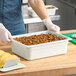 A woman using a white Cambro food pan to prepare food on a counter.