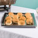 An American Metalcraft hammered stainless steel tray with rolls and dip on a table.